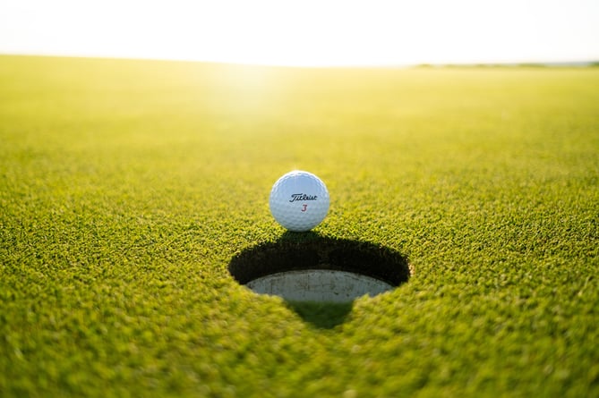 Golf ball on edge of hole at sunset.