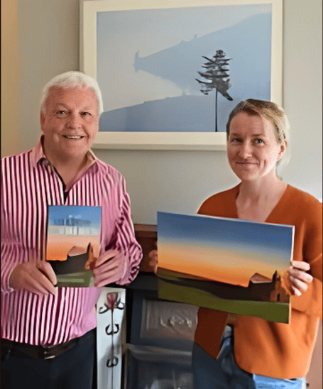 Colin Short and Kirsty Rouse with the book cover design. Behind them is a picture from Kirsty's travels in Rwanda.