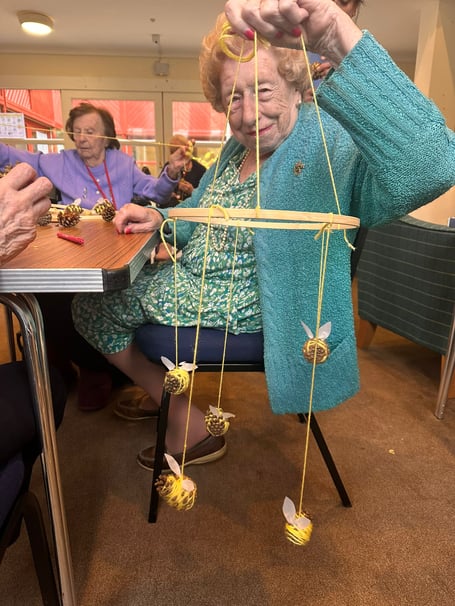 Resident Joan Edgley shows her handmade bee-decorated mobile, made of wood, string and pinecones