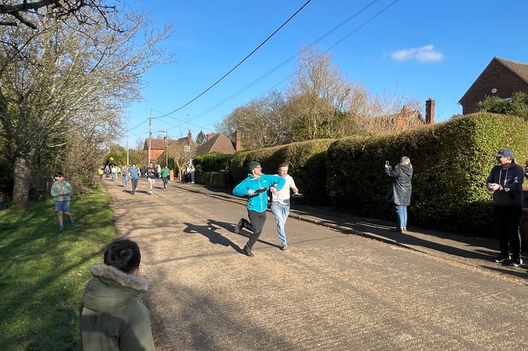 Adults taking part in the Big Elstead Pancake Race. Is that move legal? Over to a VAR review.